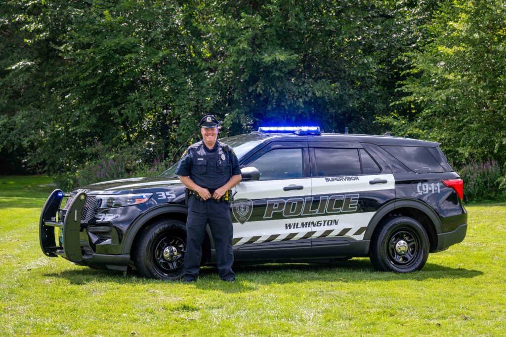 Male police officer standing in front of a cruiser.